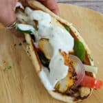 zhug feta hummus chicken wrap on a bamboo plate and folded in hand